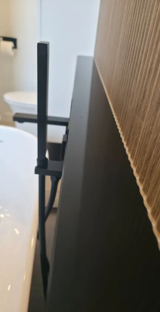 Joint de silicone parfaitement aligné entre une vanité noire et un mur de bois à lattes.