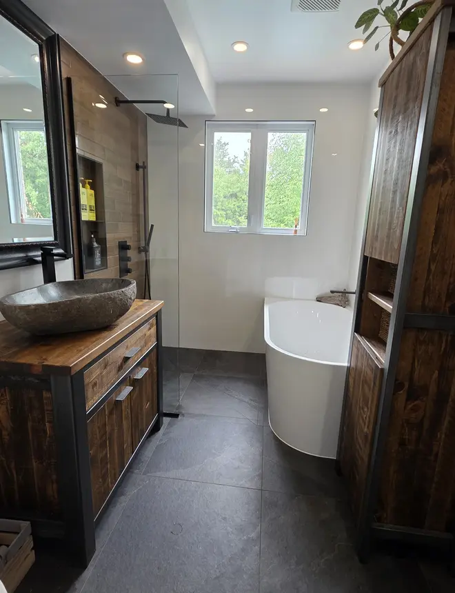 Douche italienne sans seuil avec céramique aspect bois, robinetterie noir mat et bain autoportant.